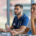 Dois estudantes, um homem jovem branco com barba e uniforme de médico azul escuro ao fundo da imagem; uma mulher jovem de pele bronzeada e cabelos castanhos lisos e presos no plano da frente estão em um ambiente de sala de aula para representar a especialização com bolsa no Ensino InCor para multiprofissionais
