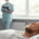 Paciente homem adulto de pele clara e cabelos louros dormindo no leito hospitalar. Ao fundo, está uma médica fazendo anotações representando a área de medicina do sono