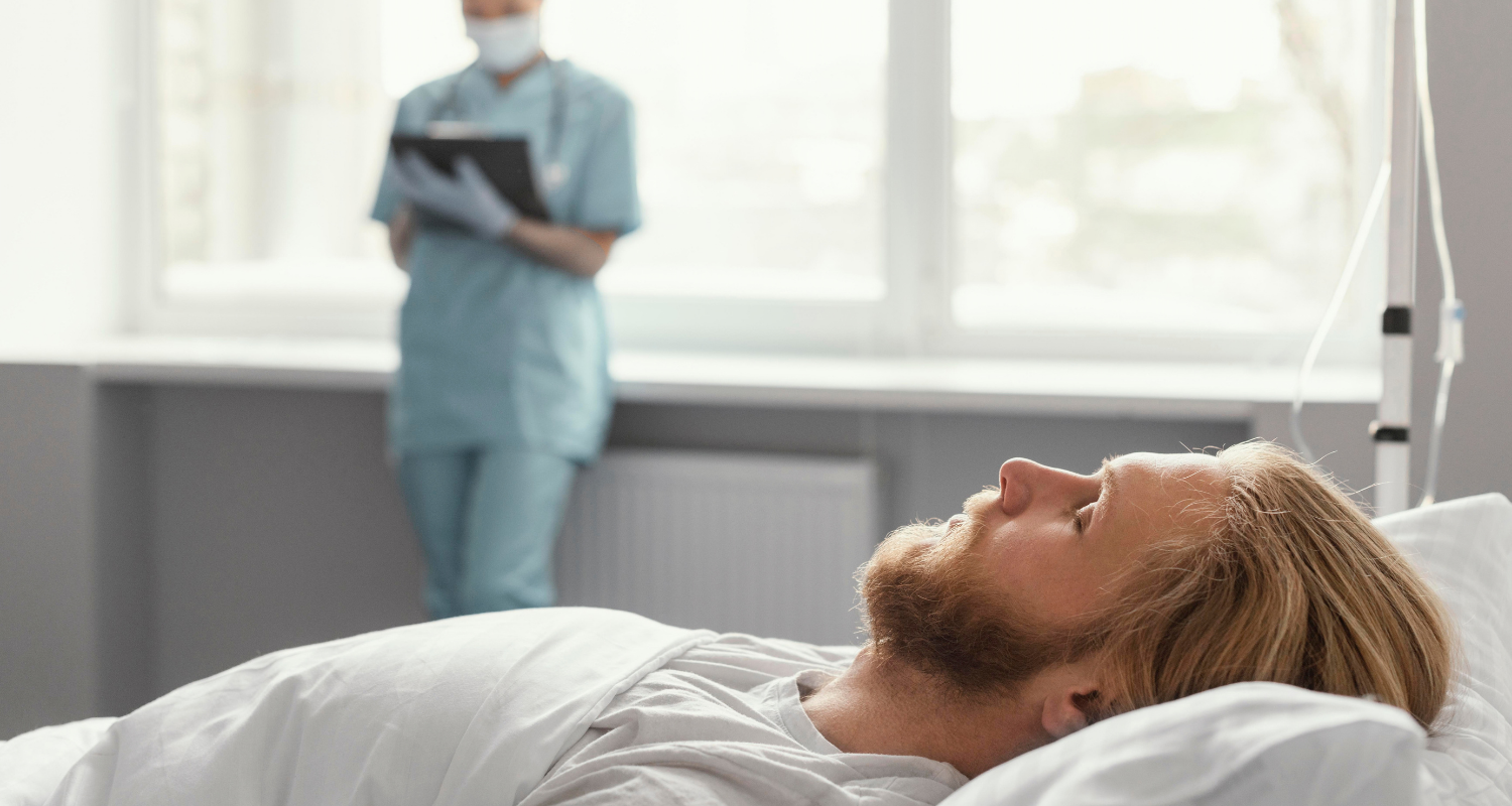 Paciente homem adulto de pele clara e cabelos louros dormindo no leito hospitalar. Ao fundo, está uma médica fazendo anotações representando a área de medicina do sono