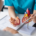 Ensino sobre miocardiopatias onde temos uma a imagem apenas das mãos de uma médica com seu uniforme azul petróleo segurando um coração de plástico com seu aluno em sua frente que usa jaleco branco. Ambos são pessoas de pele clara